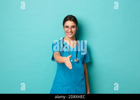 Concetto di coronavirus, pandemia e allontanamento sociale. Immagine di sicuro bella dottoressa, sorridente ed estensibile mano per stretta di mano, saluto Foto Stock