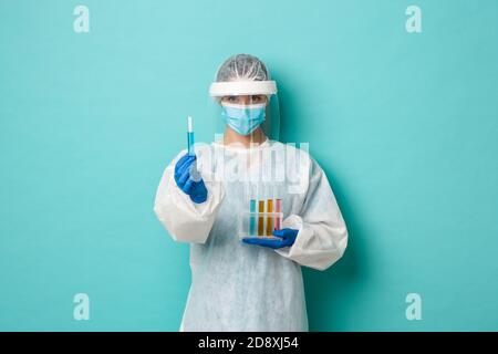 Concetto di covid-19, pandemia e salute. Lavoratore di laboratorio tecnico sicuro, indossando dispositivi di protezione individuale, tenendo provette e mostrando Foto Stock