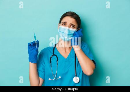 Concetto di covid-19 e concetto di quarantena. Primo piano di compassionate bella dottore femminile in maschera medica, guanti e scrub, tenendo siringa e. Foto Stock