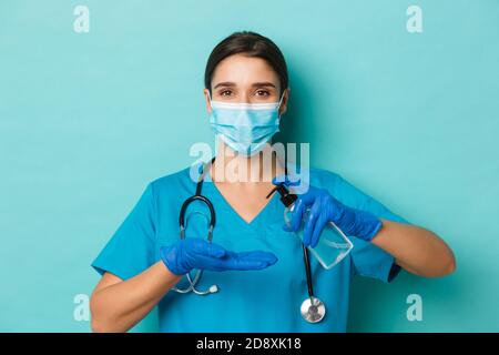 Concetto di covid-19 e concetto di quarantena. Primo piano di una bella dottoressa in maschera medica, guanti e scrub, utilizzando disinfettante per le mani, in piedi Foto Stock