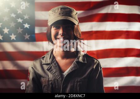 Veterans Day, Memorial Day, Independence Day. Ritratto di una soldato sorridente che si pone sullo sfondo della bandiera americana. Leggero. Foto Stock