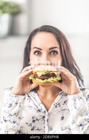 Giovane donna che tiene un hamburger davanti alla bocca. Foto Stock