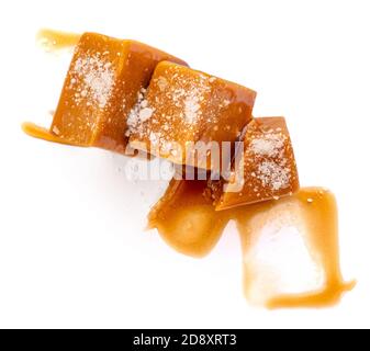 Caramelle al caramello e salsa dolce isolato su sfondo bianco, vista dall'alto. Pezzi di caramello salato fatti in casa Foto Stock