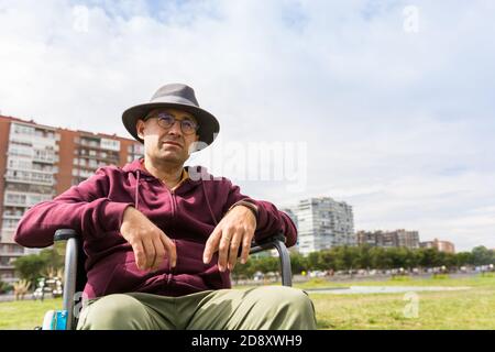 Uomo in sedia a rotelle facendo una passeggiata nel parco con una sensazione di tristezza sulla sua paralisi Foto Stock