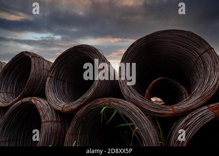 Bobina in filo d'acciaio contro cielo scuro. Acciaio metallico rinforzato per la costruzione di calcestruzzo. Filo di ferro per l'industria edile. Bobina o rotolo di acciaio argentato Foto Stock