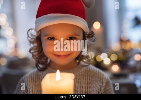 Allegra bambina con cappello di Santa al chiuso a Natale, tenendo la candela. Foto Stock