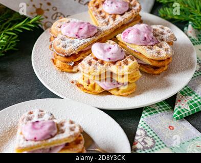 waffle appena sfornati a forma di cuore serviti su un piatto durante il natale con ripieno di crema di mirtillo e la guarnizione Foto Stock