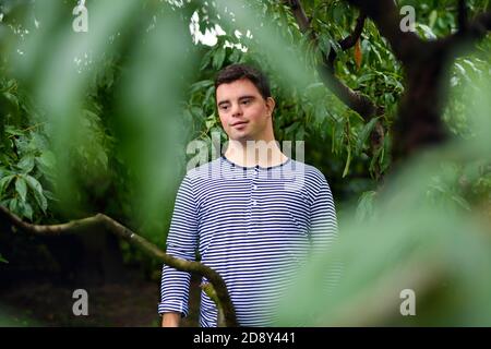 Ritratto dell'uomo adulto della sindrome di Down in piedi all'aperto sotto l'albero. Foto Stock