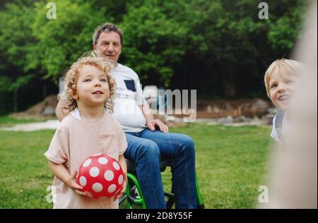 Bambini piccoli con nonni anziani in sedia a rotelle che giocano. Foto Stock