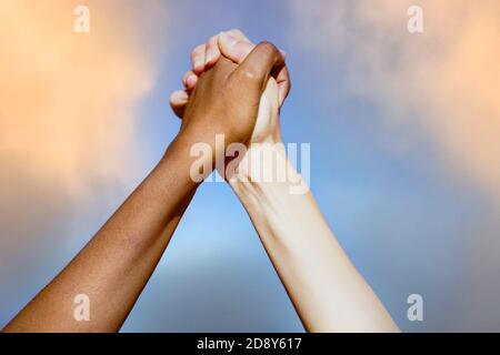 Le mani multietniche delle donne insieme contro il cielo nuvoloso. Foto Stock