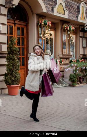 La donna felice tiene i sacchetti di carta con il simbolo di vendita nei depositi con le vendite a Natale, intorno alla città. Concetto di shopping, vacanze, felicità Foto Stock
