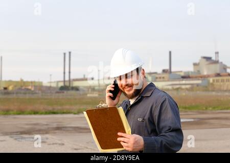 Ritratto di caucasio caucasiano sul cantiere, parlando da walkie talkie e tenendo carte. Foto Stock