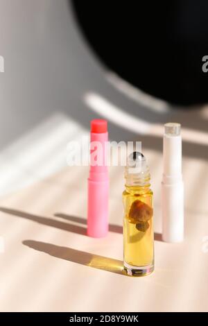 Flacone a rullo trasparente e rossetto igienico su sfondo ombreggiato a strisce. Foto Stock