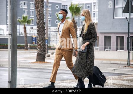 Coppia di lavoro che indossa maschere Crossing Street durante il viaggio d'affari con Bagagli durante la salute Pandemic Foto Stock