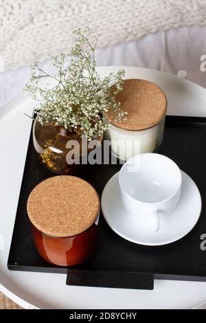 Candele profumate, una tazza bianca e fiori su un vassoio di metallo vicino al letto. Interni accoglienti Foto Stock