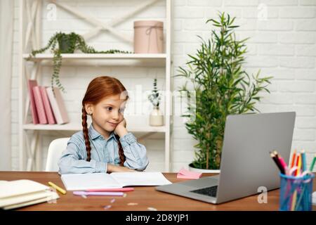 felice bambina che usa il laptop per studiare il sistema di apprendimento online. bambino ascolta attentamente l'insegnante. lezione online a casa Foto Stock