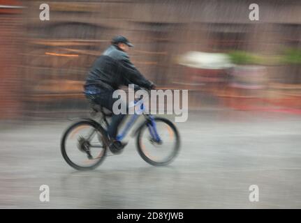 Giù. Il ciclista bagnato corre per le strade in una giornata piovosa . Sfocatura intenzionale del movimento Foto Stock