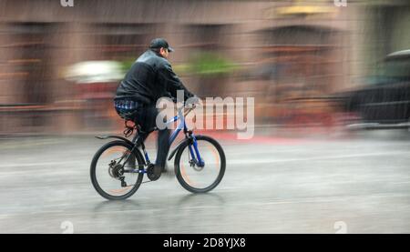 Giù. Il ciclista bagnato corre per le strade in una giornata piovosa . Sfocatura intenzionale del movimento Foto Stock