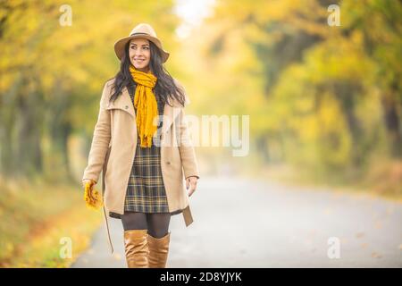 Femmina sorridente con una passeggiata autunnale all'aperto circondata da alberi gialli. Foto Stock