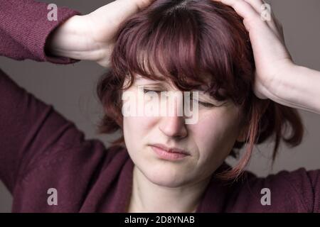 Donna dai capelli rossi con mal di testa. Espressione facciale umana, emozione, sensazione, segno linguaggio del corpo simbolo Foto Stock