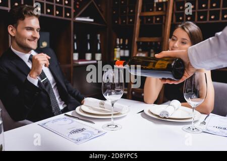 Fuoco selettivo del sommelier che versa il vino vicino alla coppia elegante dentro ristorante Foto Stock