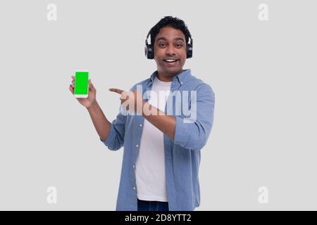 Indian Man ascoltare la musica dal telefono che punta ad esso. L'uomo canto alla musica. Uomo che punta alla schermata verde del telefono. Isolato Foto Stock