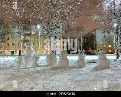 Un'azienda di una varietà di snowmen innevati. Grande e piccola, spaventosa e divertente, una in una maschera medica protettiva. Foto Stock