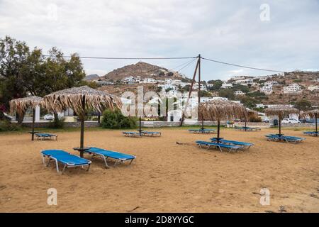 Chora, Isola di iOS, Grecia - 19 settembre 2020: Vista della spiaggia sabbiosa sull'isola greca di iOS lettini e ombrelloni. Città sullo sfondo. Giorno nuvoloso Foto Stock