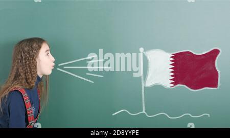 Ragazza pre-adolescente che soffia sul bordo della scuola disegnata sulla bandiera del Qatar lavagna. Foto ad alta risoluzione. Profondità di campo completa. Foto Stock