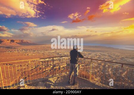 Giovane uomo in piedi su un punto panoramico sul monte (Masada) e osservare l'alba sul Mar Morto. Regione del Mar Morto, Masada, Israele Foto Stock