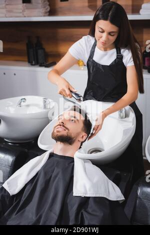 giovane parrucchiere lavando i capelli del cliente in salone di bellezza Foto Stock