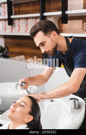 giovane barbiere bearato lavarsi i capelli della donna in salone di bellezza Foto Stock