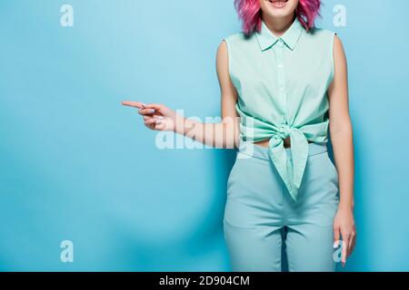 vista ritagliata della giovane donna con i capelli rosa che puntano da parte su sfondo blu Foto Stock