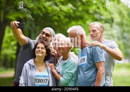 Gruppo di amici anziani felici che partecipano alla maratona estiva gareggia insieme nel parco forestale scattando foto selfie di gruppo Foto Stock