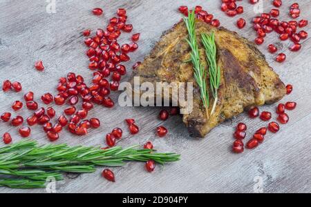 bistecca alla griglia su fondo ligneo. pezzo di carne fritta con semi di melograno e un rametto di rosmarino. Foto Stock