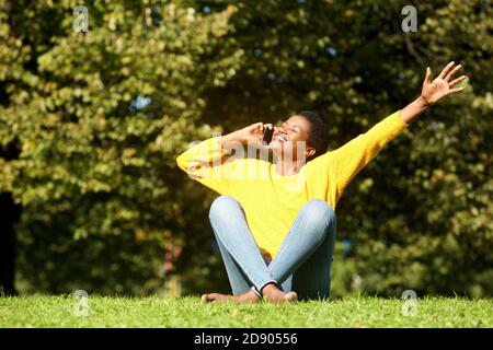 Ritratto di felice afroamericana che strega nel parco e. parlare sul cellulare Foto Stock