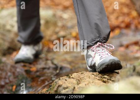 Primo piano di un trekking gambe indossare scarpe da trekking attraversamento un torrente in autunno in una foresta Foto Stock