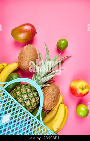 Borsa della spesa della drogheria con frutta esotica biologica su sfondo rosa. Piatto di varietà di frutta tropicale fresca che si spillano da una borsa riutilizzabile. Foto Stock