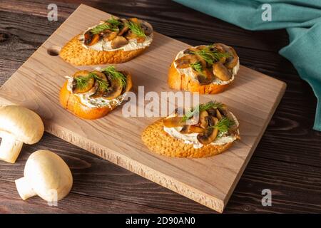 Baguette toast con formaggio cremoso e funghi su una tavola di legno. Spuntini, colazioni veloci. Foto Stock