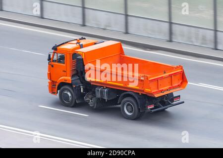 Un autocarro con cassone ribaltabile arancione con cassone vuoto e un la spazzola per la pulizia della strada si muove in autostrada Foto Stock