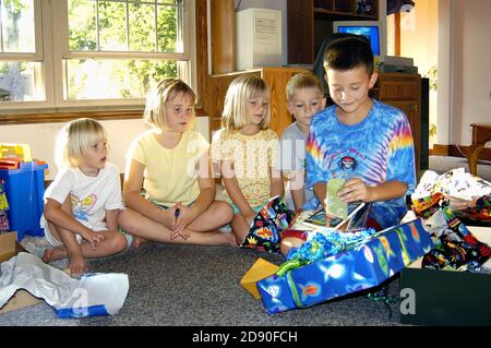 il ragazzo di 9 anni festeggia il compleanno con gli amici condividendo i regali e una torta con le candele Foto Stock