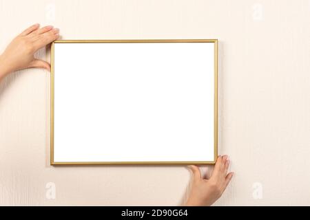 Donna che sta mettendo il mockup della cornice sulla parete. Cornice della mano è appesa alla parete. Giovane donna con cornice vuota con copyspace Foto Stock