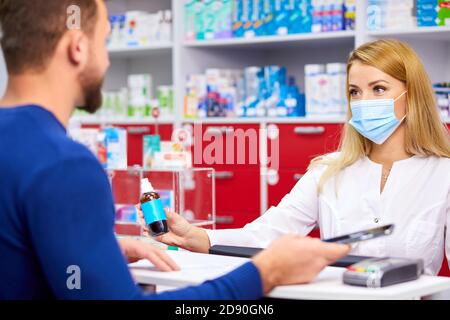 giovane professionista dract dare farmaci al cliente in farmacia moderna, consultare e raccomandare, indossare maschera medica di protezione dal coronavirus covid-19 Foto Stock