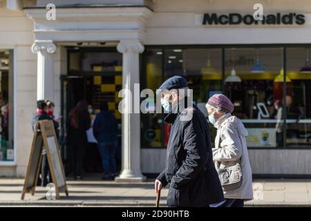 La coppia anziana che indossa maschere facciali passa accanto al McDonalds a Leamington Spa, Warwickshire, mentre un altro mese lungo il blocco telai per il Regno Unito Foto Stock