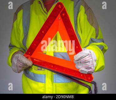 Guardaroba di un uomo che indossa guanti e giacca di sicurezza in pile giallo fluorescente ad alta visibilità, con un triangolo segnaletico arancione riflettente. Foto Stock