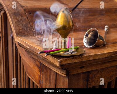 Closeup POV shot di bastoni tradizionali di incenso / bastoni di joss in un supporto di ottone su un'unità etnica di legno, con fumo aromatico / profumato aumento. Foto Stock