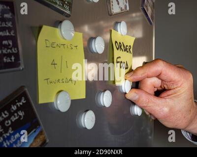 Chiusura di una mano di un uomo che attacca una nota per ordinare cibo su una porta di frigorifero, utilizzando magneti. Foto Stock