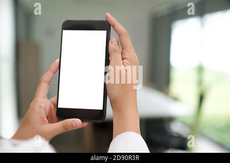 Un'immagine ritagliata di mani che tengono lo smartphone mock-up con schermo vuoto in ufficio. Foto Stock