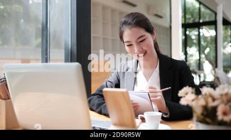 Ritratto dell'esecutivo femminile che pensa al programma di lavoro per il dipendente che scrive il rapporto nel notebook mentre usa il computer portatile. Foto Stock