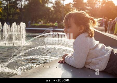 adorabile bambina guarda le fontane nel parco nel parco in una giornata di sole Foto Stock